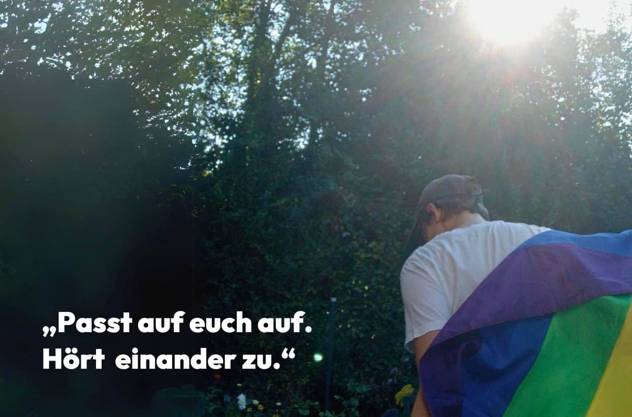 Mann mit Regenbogenflagge im Wald, Zitat: Passt auf euch auf