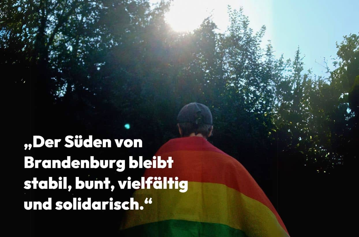 Mensch mit Regenbogenfahne im Wald