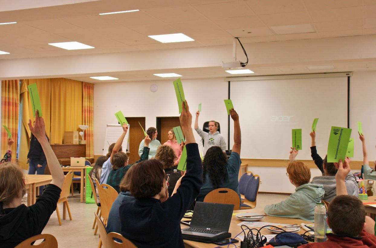Menschen heben grüne Karten in einem Seminarraum.