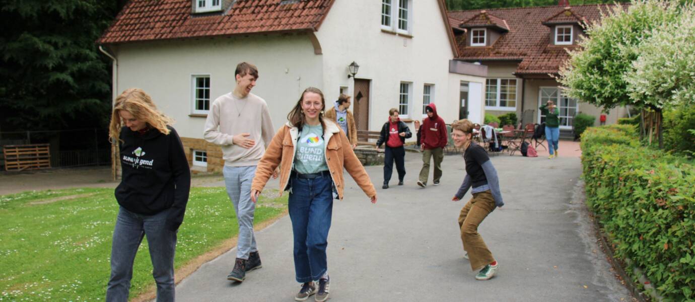 Junge Menschen spazieren fröhlich vor Landhaus.