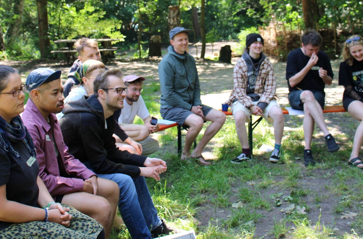 Menschen sitzen draußen auf Bänken im Kreis.