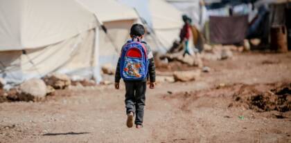 Kind mit Rucksack geht durch ein Geflüchtetenlager.