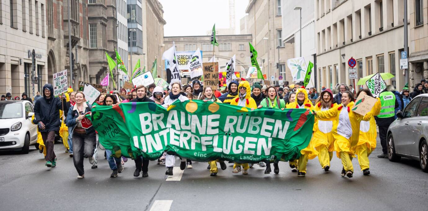 Rennende BUNDjugend-Demonstranten in bunten Kostümen mit Banner.